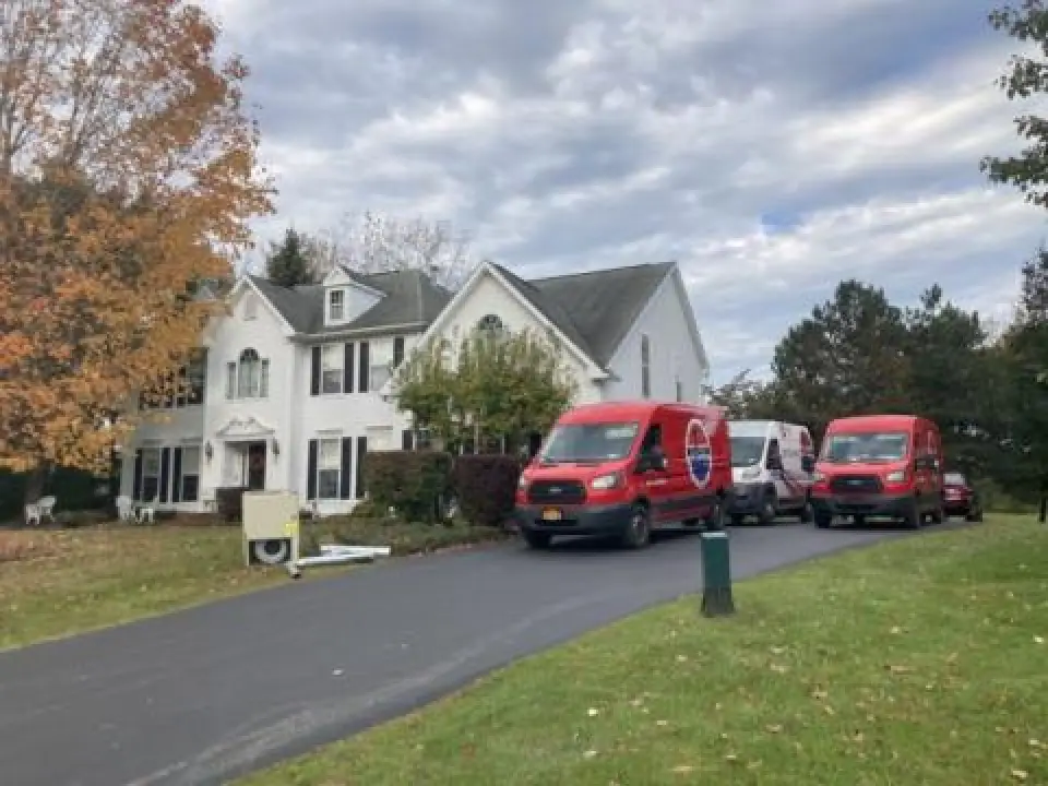 Several Empire Heating & Air Conditioning vans in the driveway of a white house. 