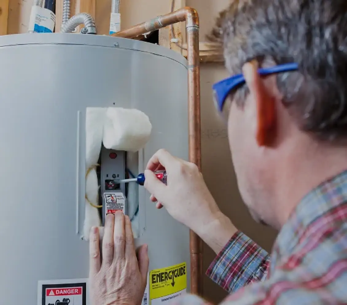 Technician adjusting a water heater control panel with a screwdriver.