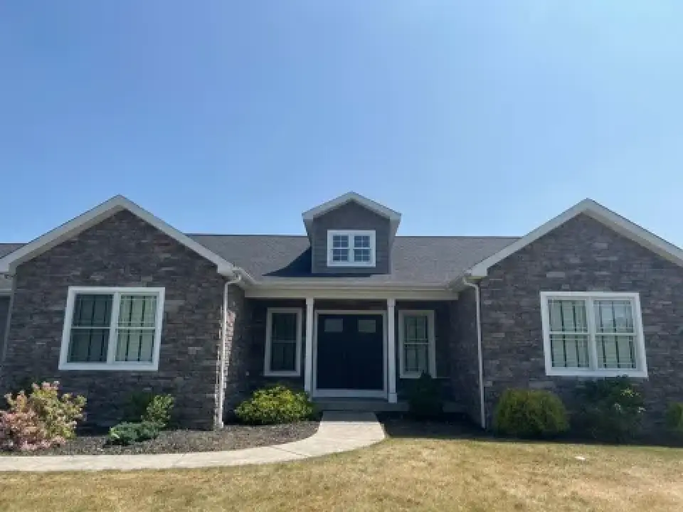 Brick home with a gray shingle roof and central dormer.