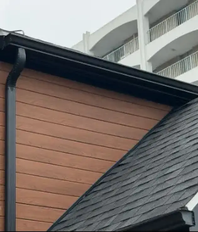 Black seamless aluminum gutter and downspout installed along the roofline of a home with woodgrain siding