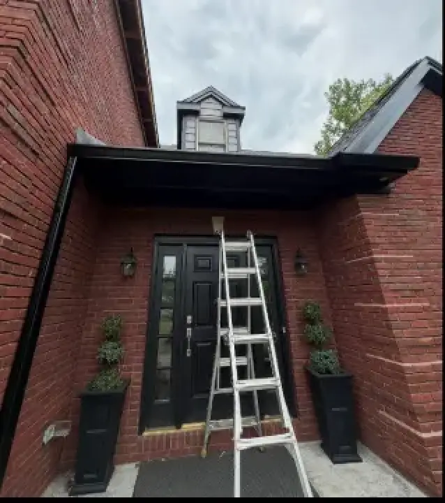 Newly installed black gutters and fascia above the front entry of a brick home