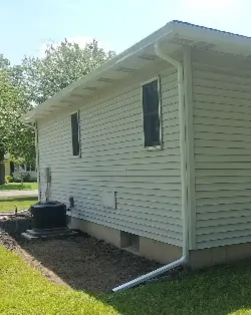 White gutter and downspout directing roof runoff away from the foundation of a vinyl-sided home