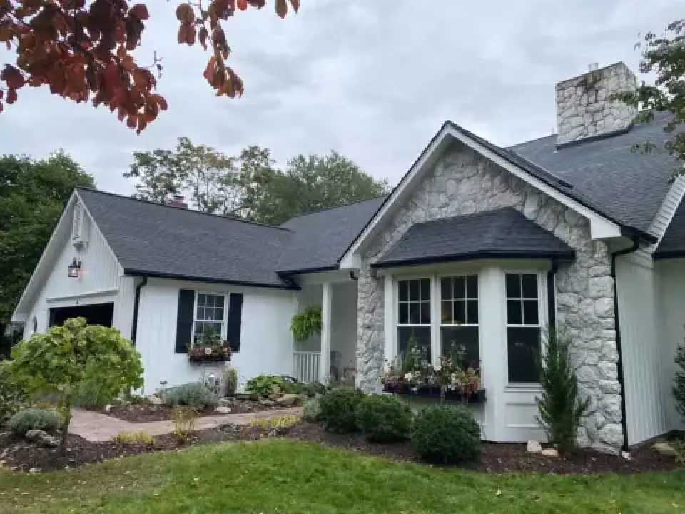 White house with dark asphalt shingle roof and stone accents.