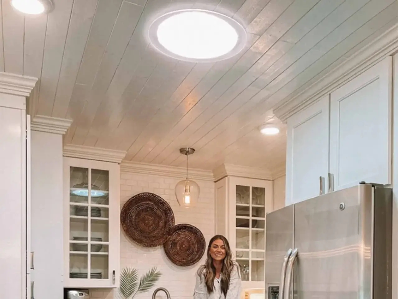 Sun tunnel brightening a white kitchen with a vaulted wood-paneled ceiling.