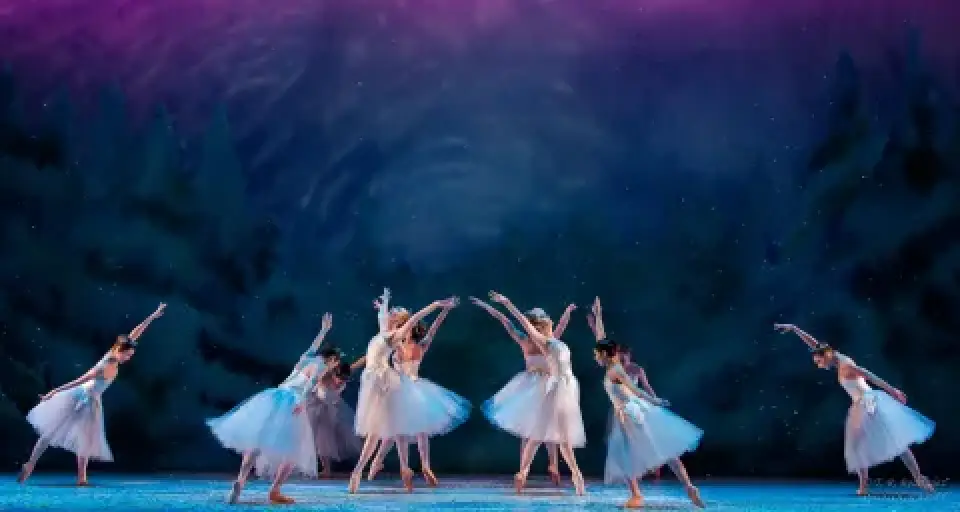 Ballerinas in white tutus dance across a blue-lit Nutcracker stage.