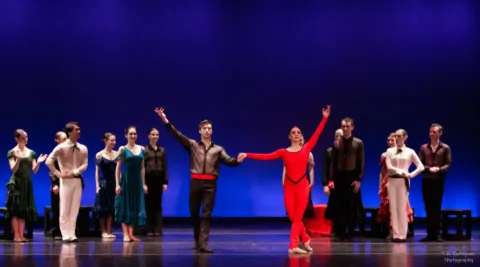 Carmen ballet cast poses onstage under blue lighting.
