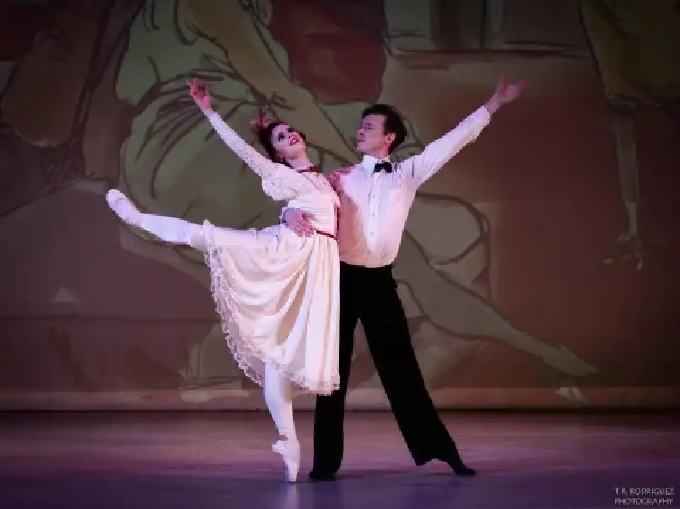 Two dancers perform a partnered pose on the Moulin d'Paris stage.