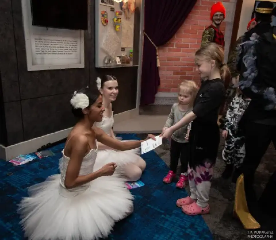 Rochester City Ballet dancers in white tutus greet children at an event.