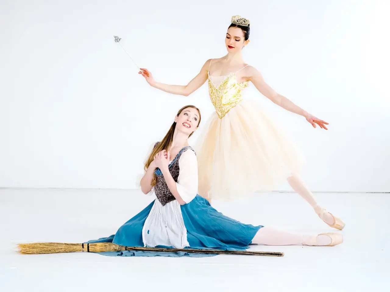 Ballerinas portray Cinderella and the Fairy Godmother with a broom and wand.