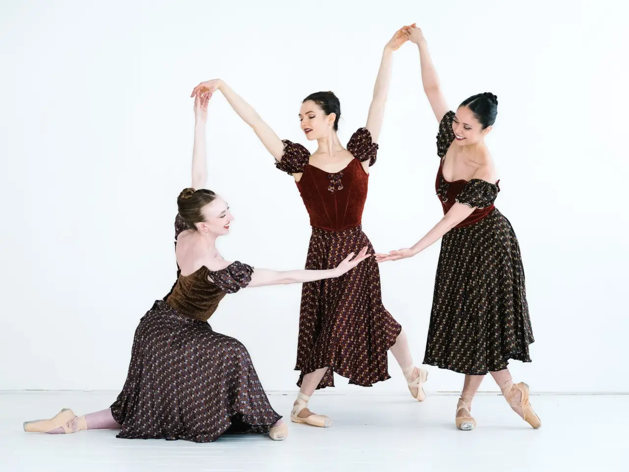 Three ballet dancers pose in flowing patterned dresses.