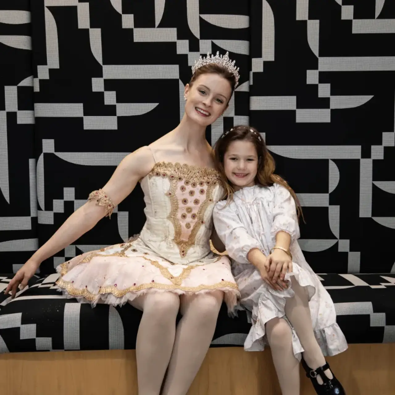 Rochester City Ballet's Sugar Plum Fairy, in a tiara and jeweled tutu, smiling beside a young guest in a party dress