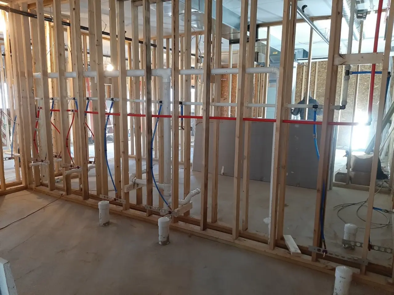 Exposed plumbing and electrical lines within the wood framing of a commercial building under construction.