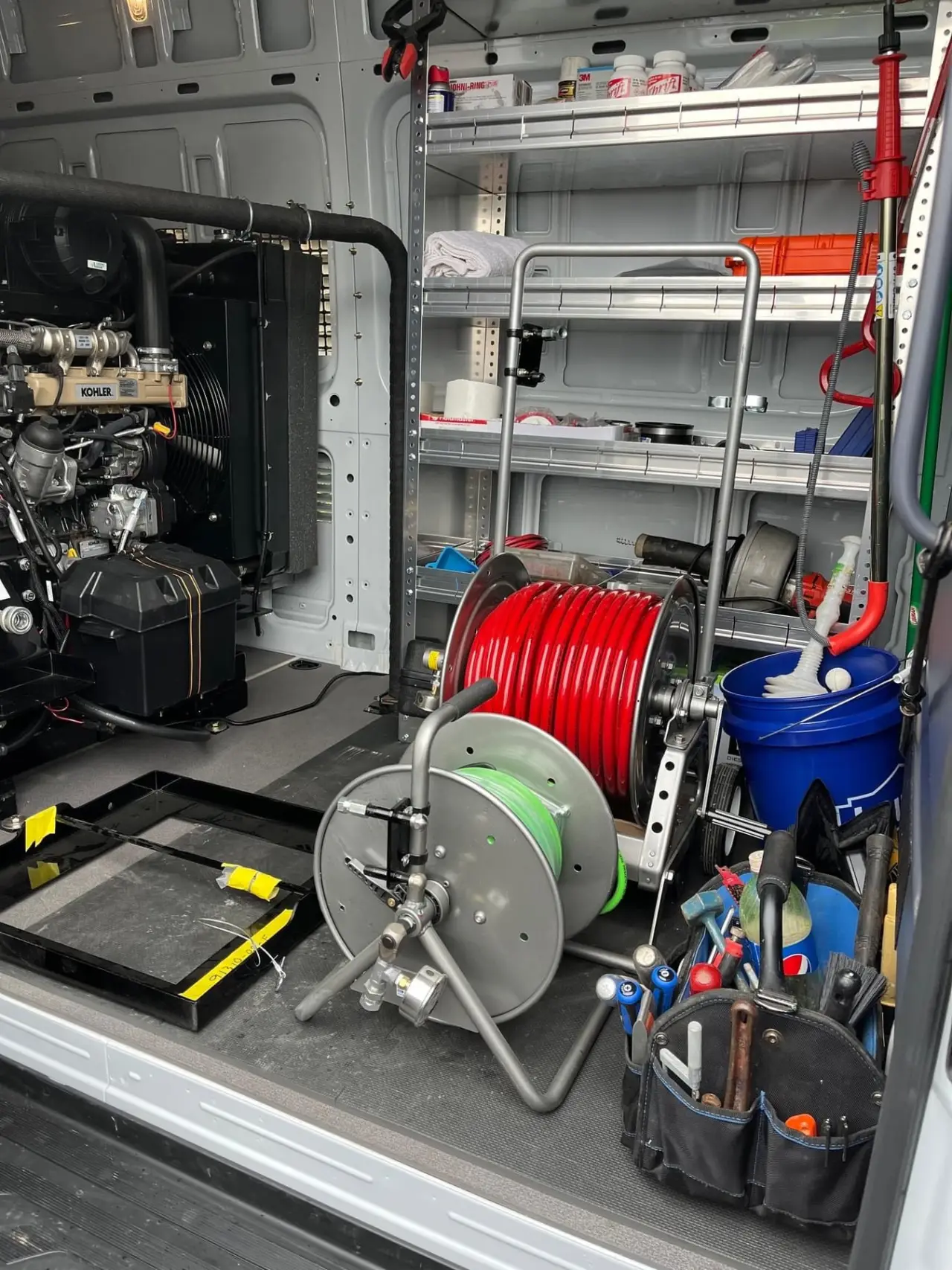 Van interior with hose reels, tools, shelves, and cleaning equipment organized neatly inside.