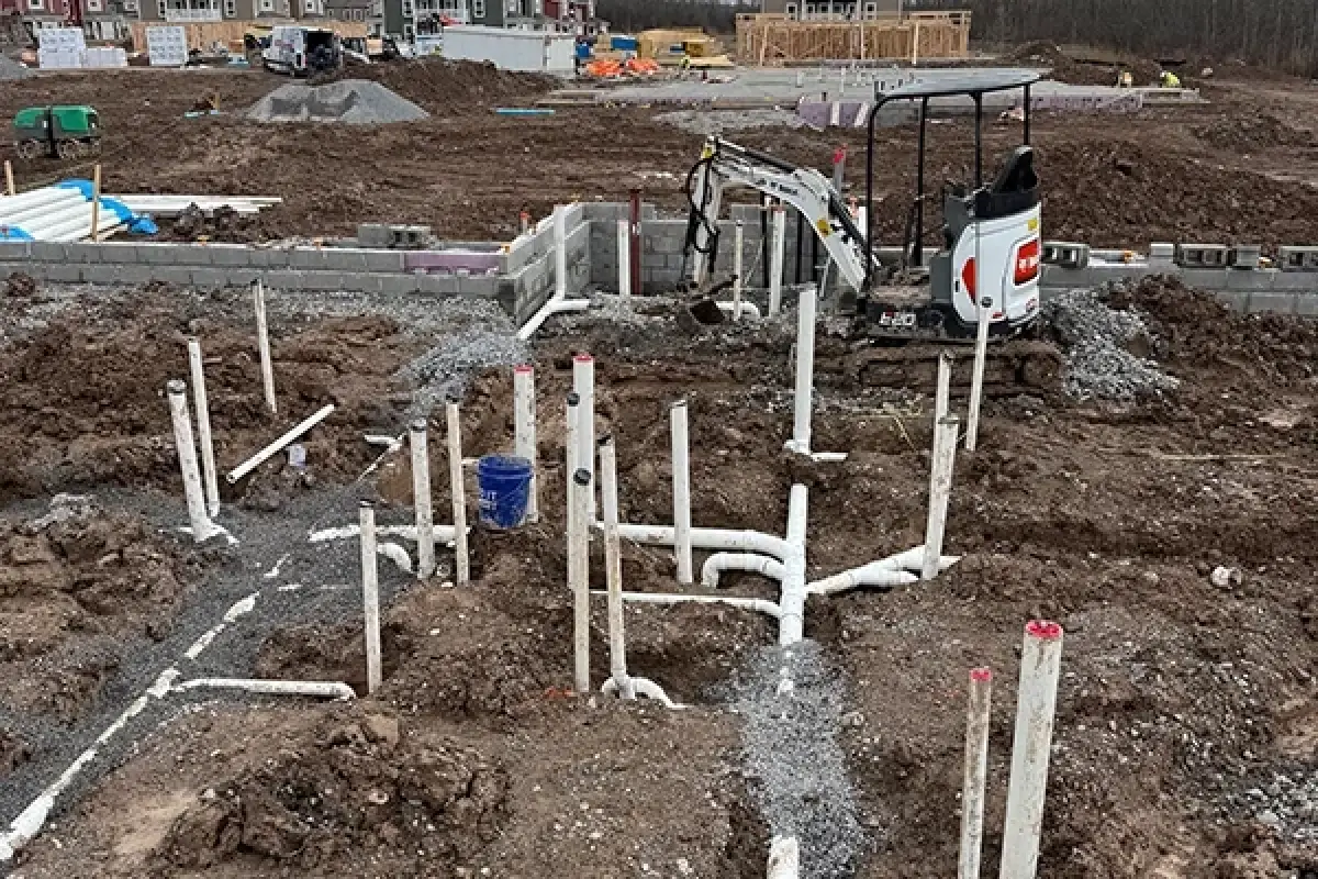 Plumbing pipes and a mini excavator at a muddy commercial construction site.