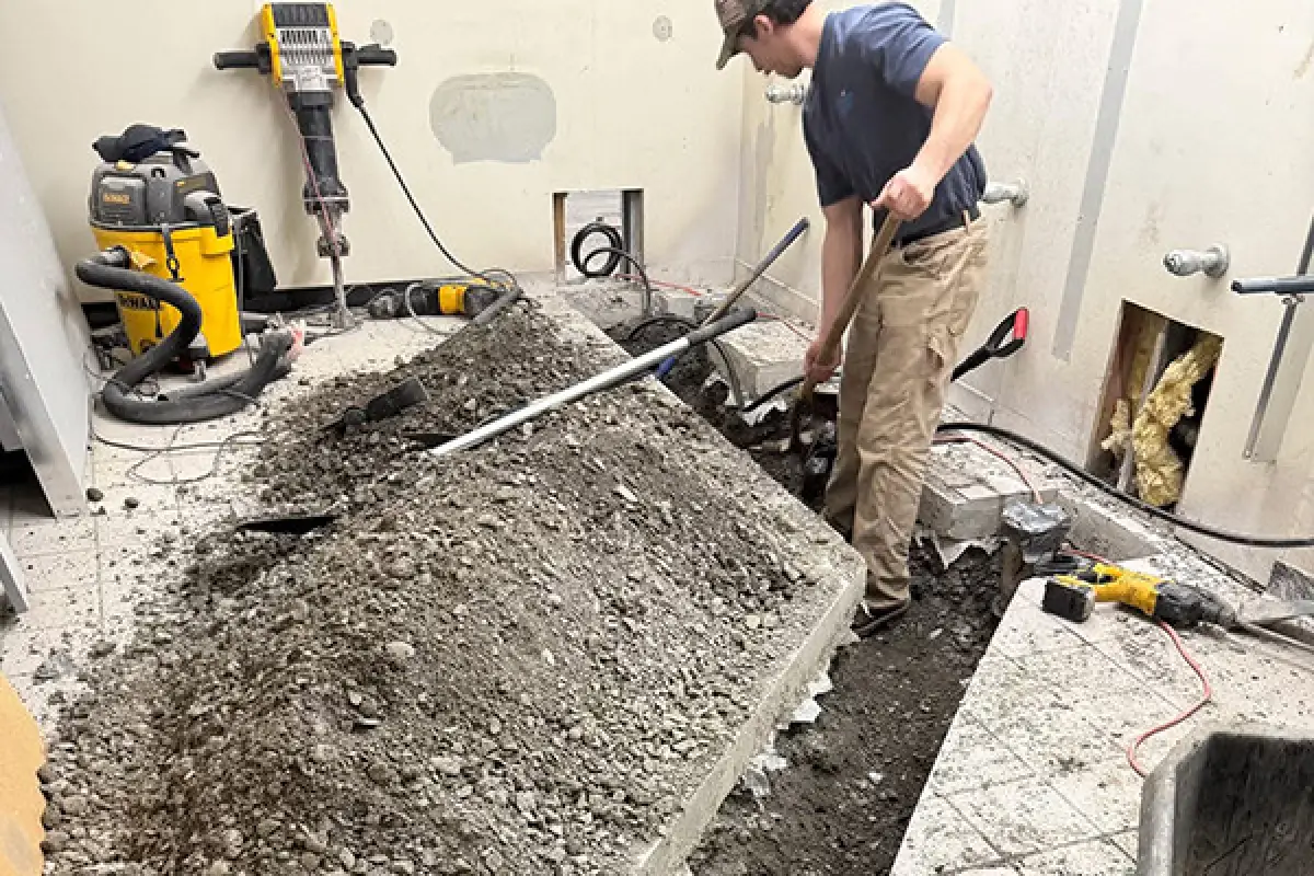 Worker digging up a tiled floor during a commercial plumbing repair project.