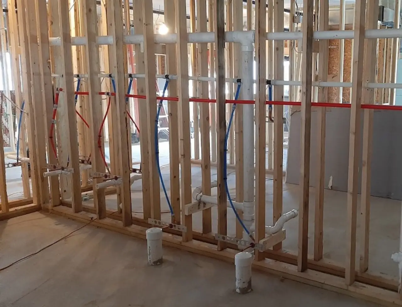 Framed wall with exposed plumbing pipes for sinks in a building under construction.