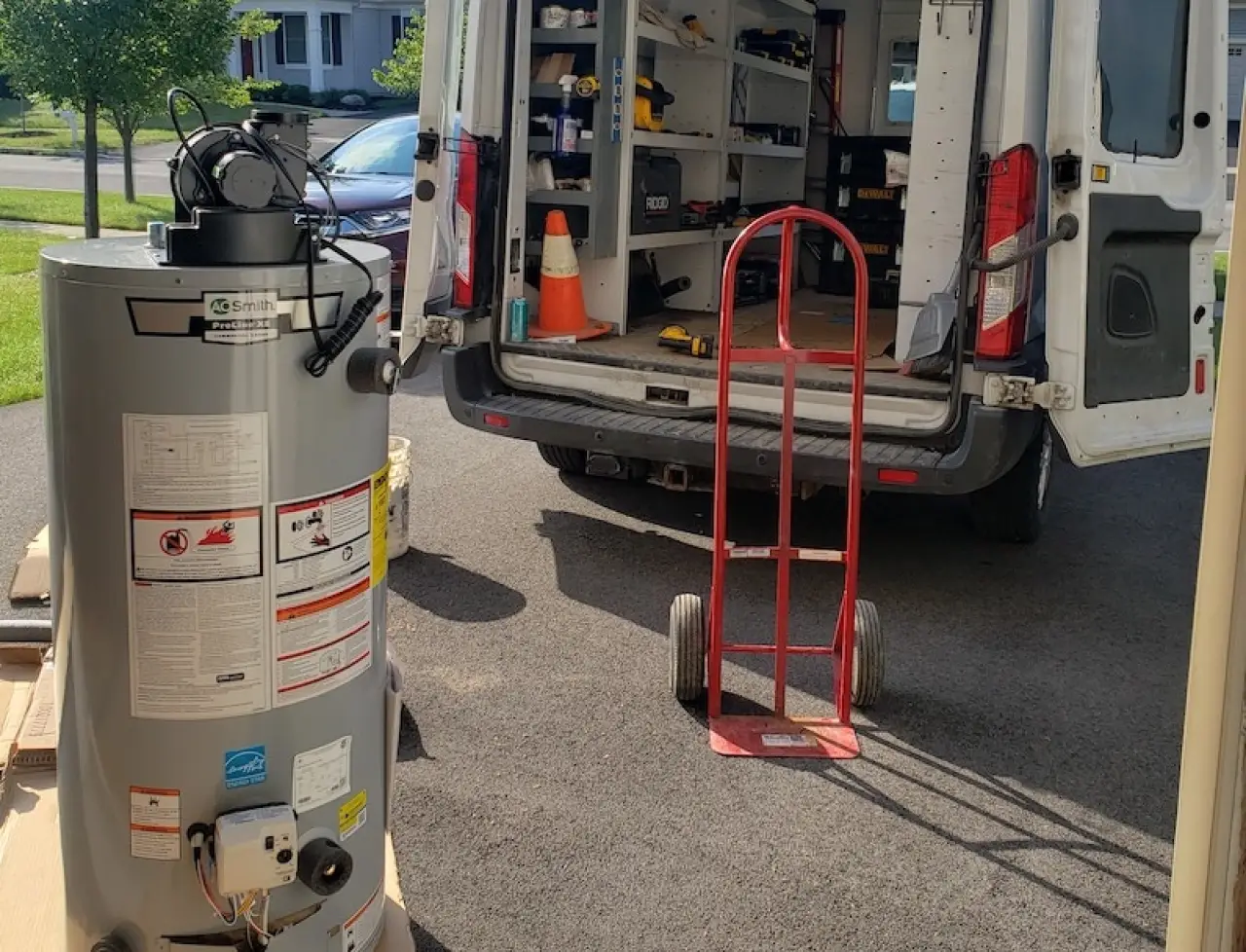 A water heater, dolly, and tools are set up near an open van parked in a driveway.