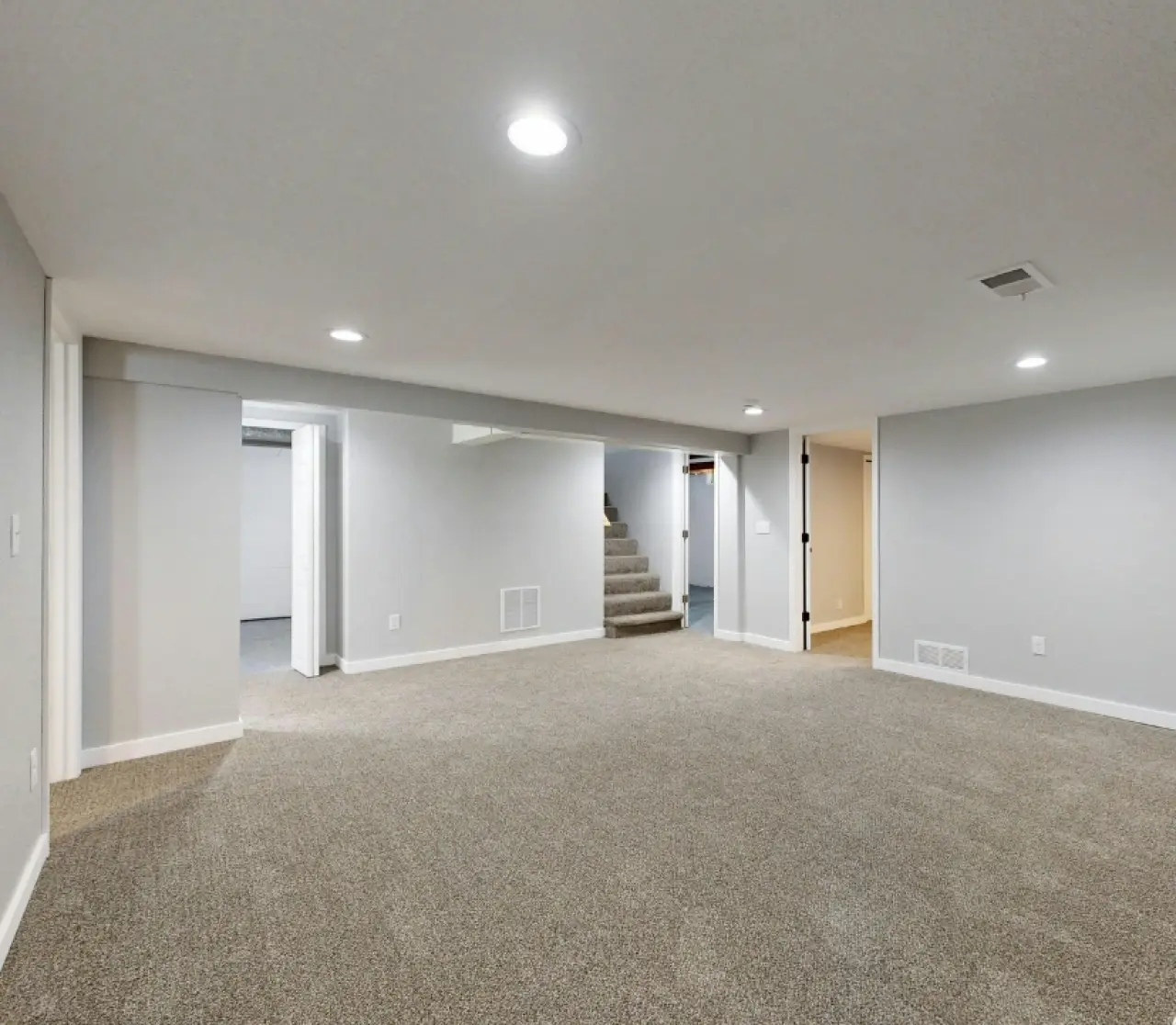 Spacious finished basement with beige carpet, recessed lights, stairs, and white walls.