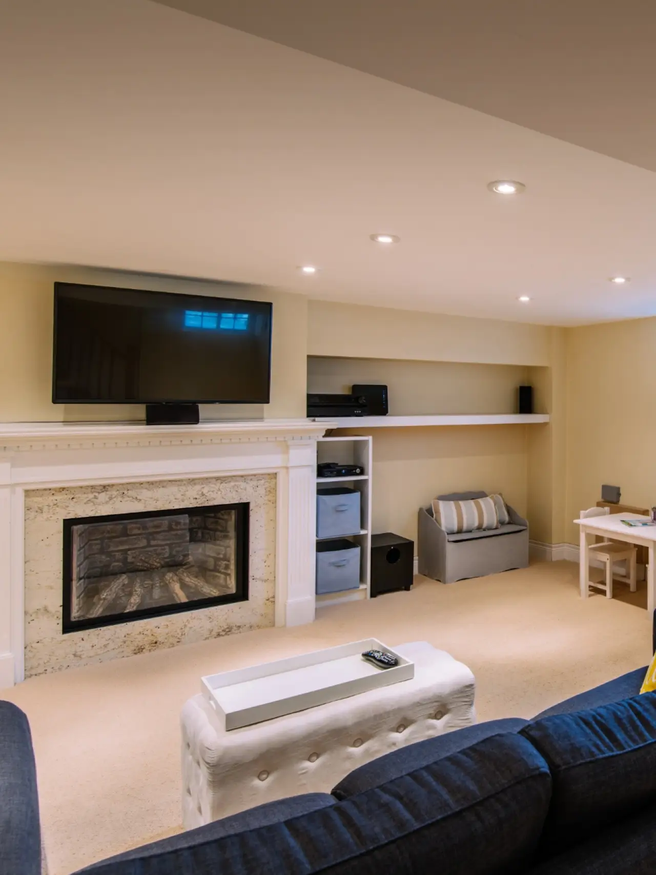 Cozy living room with fireplace, TV above mantel, shelves, and small desk in the corner.