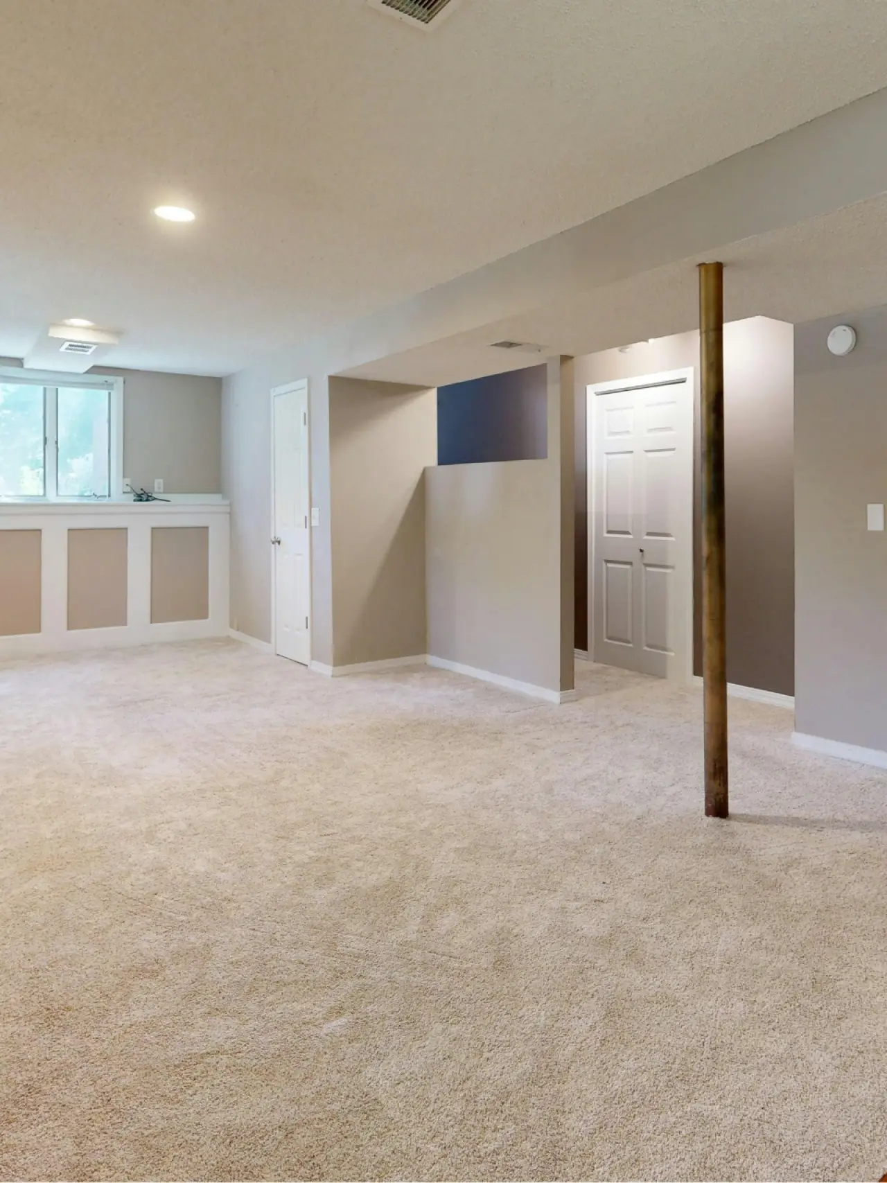 Spacious finished basement with beige carpet, white trim, a support pole, and closed doors.