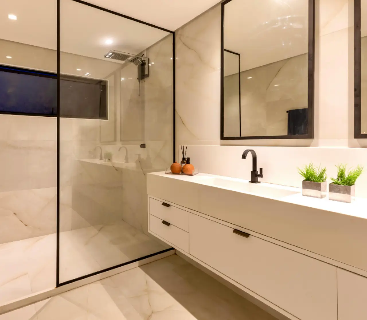 Modern bathroom with glass shower, white vanity, black faucet, mirror, and small plants.