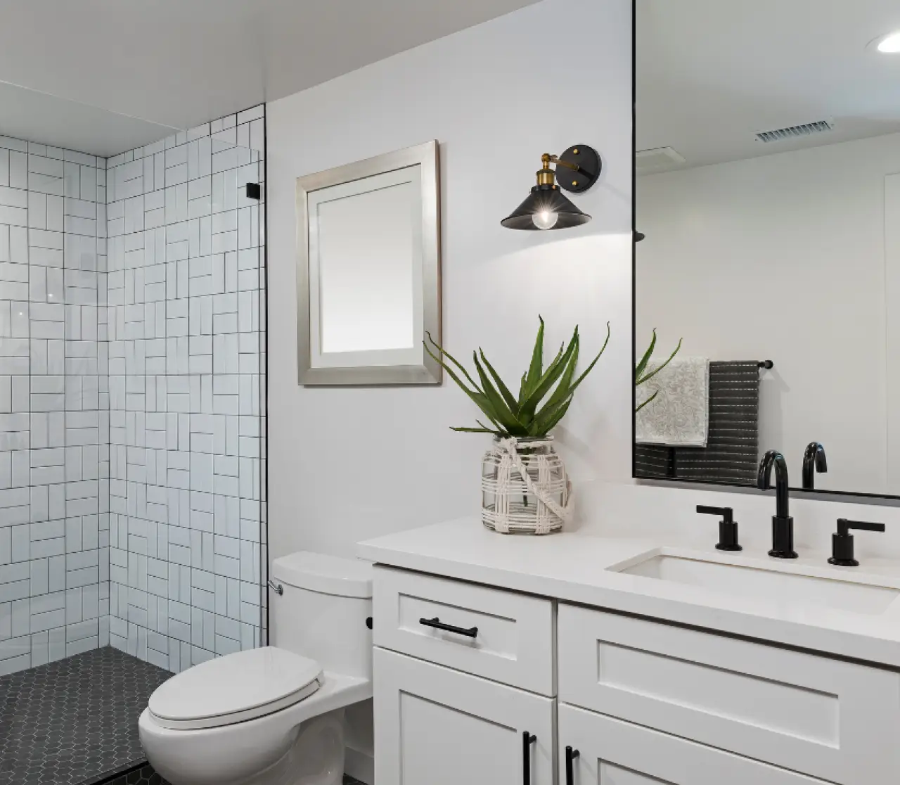Modern bathroom with white cabinets, black fixtures, a potted plant, and glass shower enclosure.