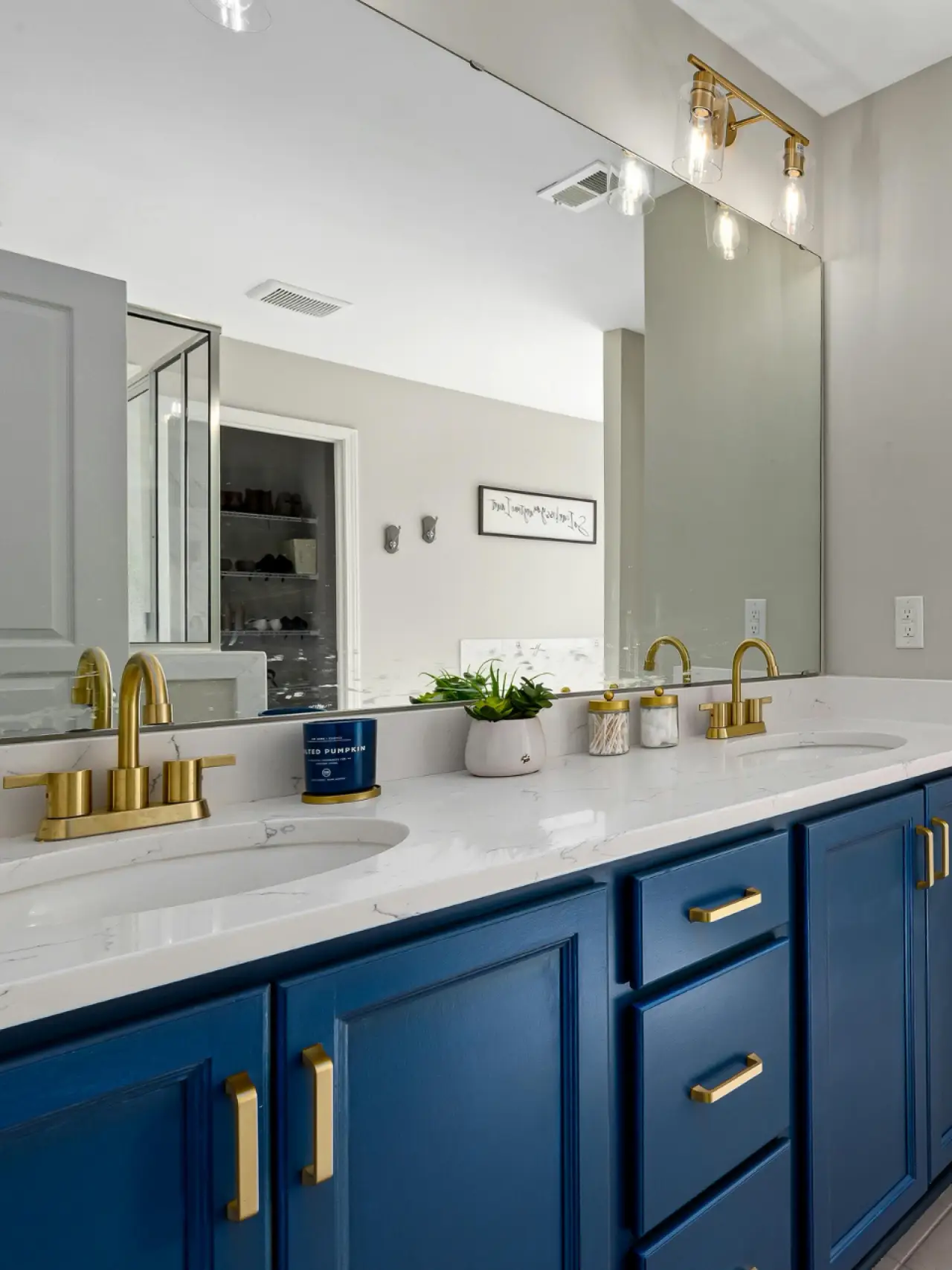 Modern bathroom with blue vanity, gold fixtures, double sinks, and a large mirror above.