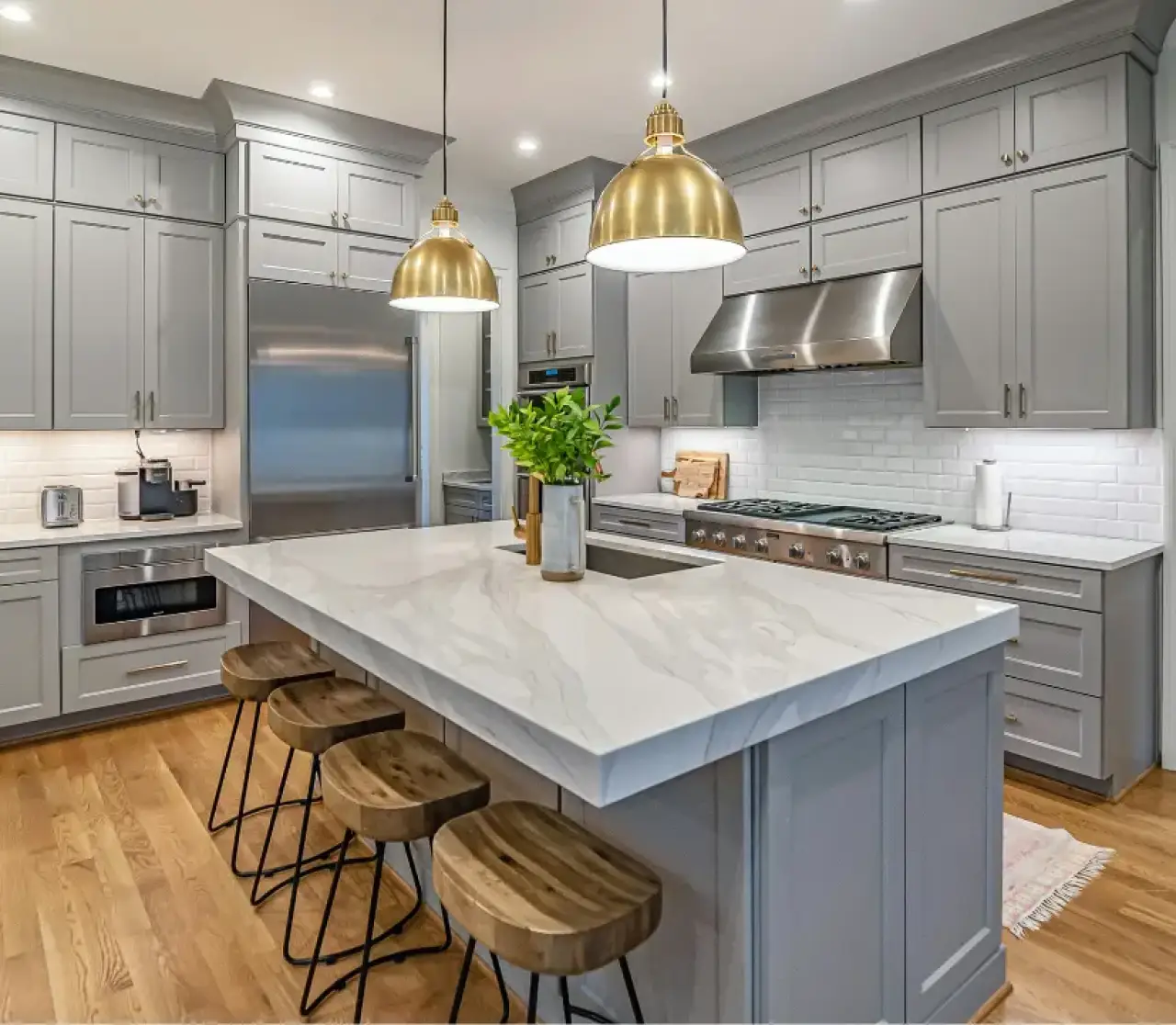 Modern gray kitchen with a marble island, wood stools, gold pendant lights, and stainless appliances.