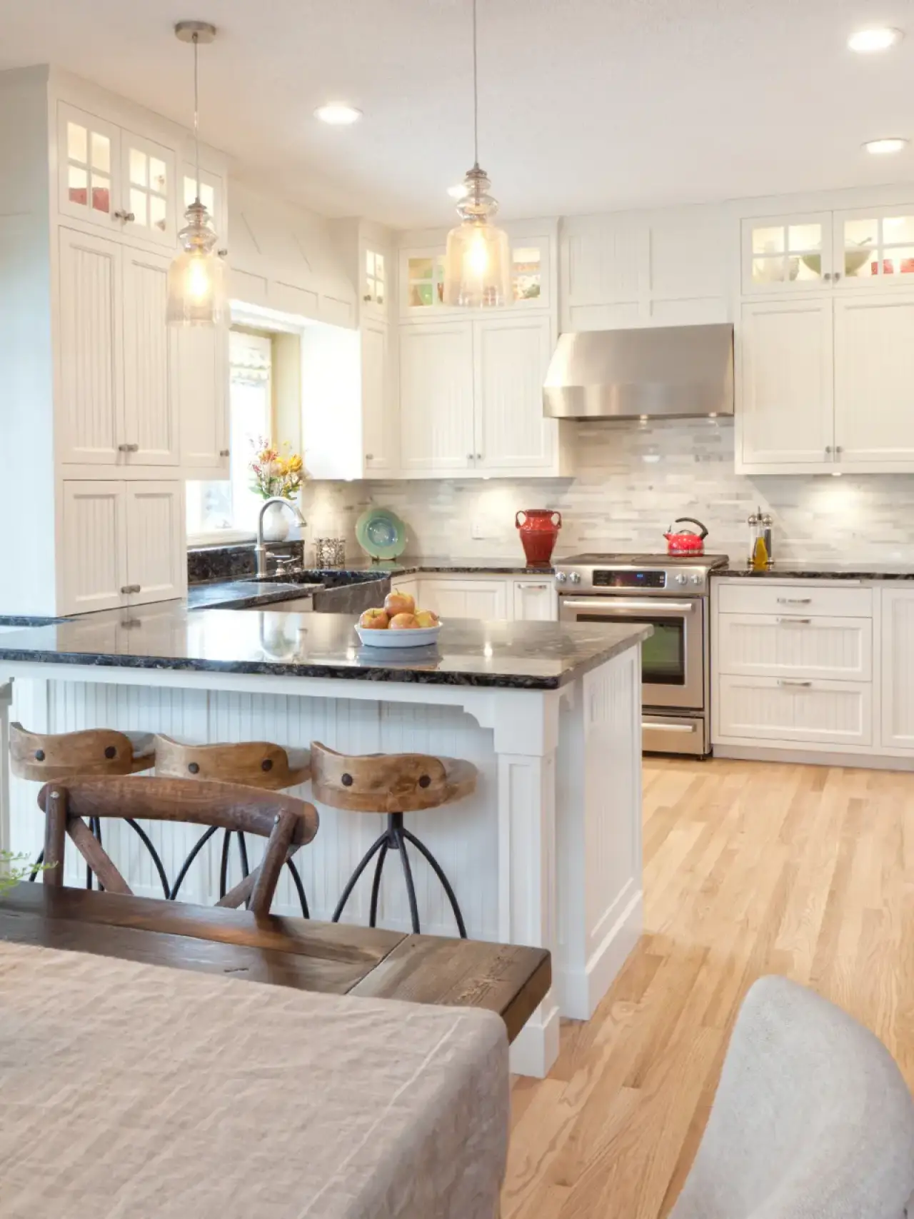 Bright, modern kitchen with white cabinets, black island, and wooden stools on light wood floor.