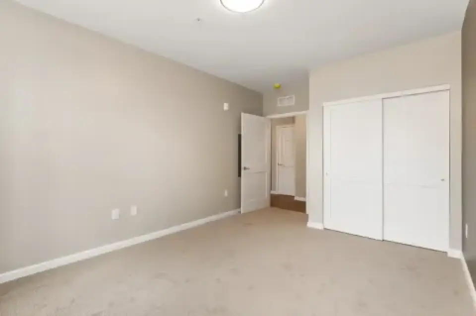 Unfurnished bedroom with beige carpet and white closet doors.