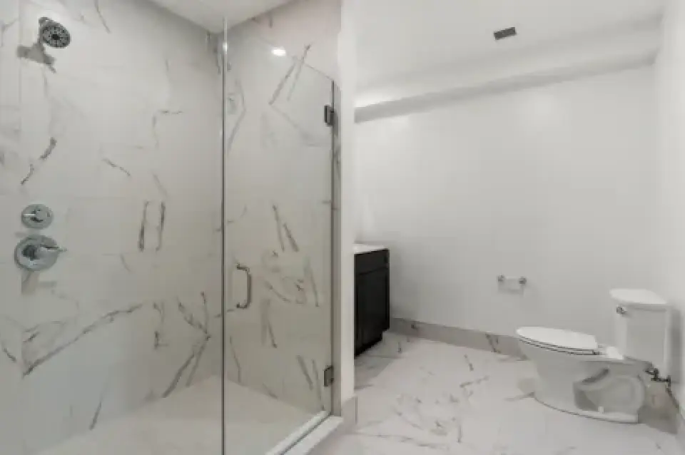 Bathroom with glass shower, marble-look tile, toilet, and vanity.