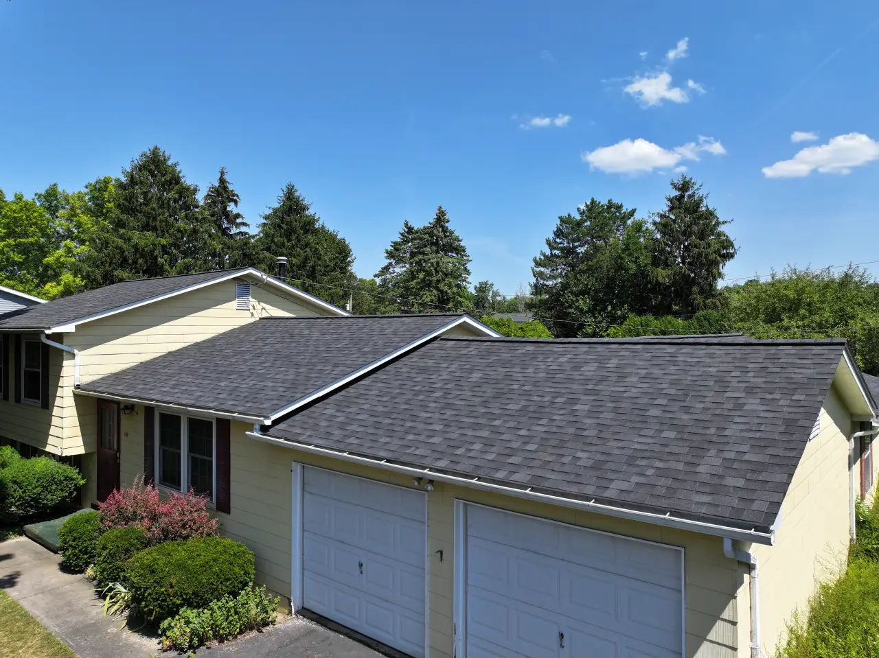 New dark shingle roof on a yellow Rochester home and garage.