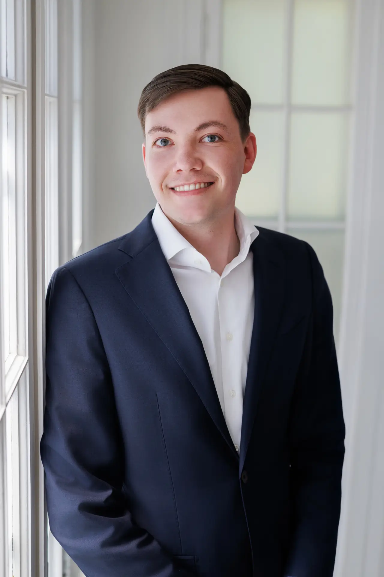 Smiling man in a blue suit with arms crossed, standing against a plain light background.