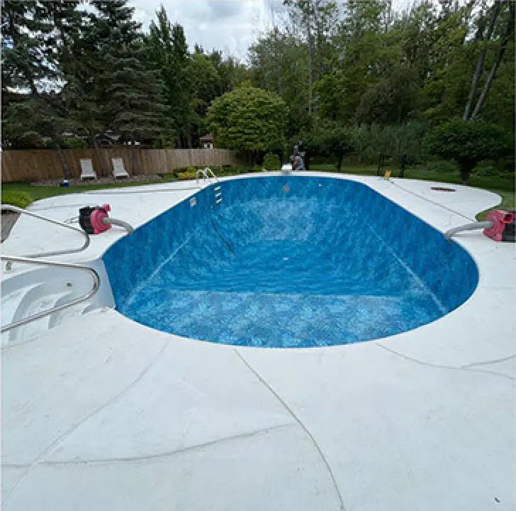 A nearly empty in-ground pool with a blue liner, surrounded by a white concrete deck.