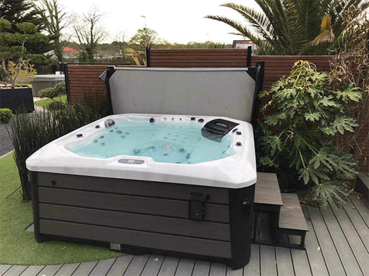 Outdoor hot tub with clear water, surrounded by plants and wooden steps on a deck.