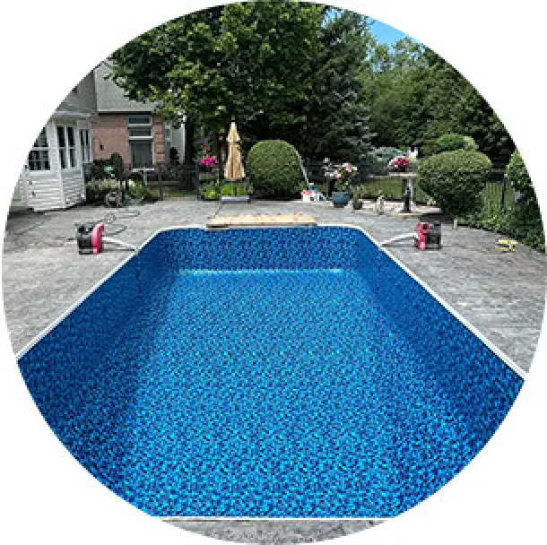 An empty in-ground pool with a blue patterned liner in a backyard surrounded by greenery.