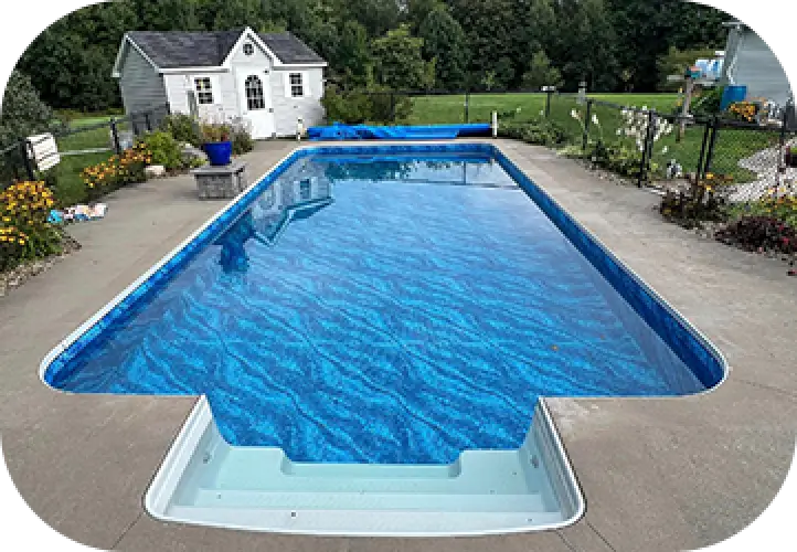 Rectangular backyard pool with clear blue water, surrounded by flowers and a small white shed.