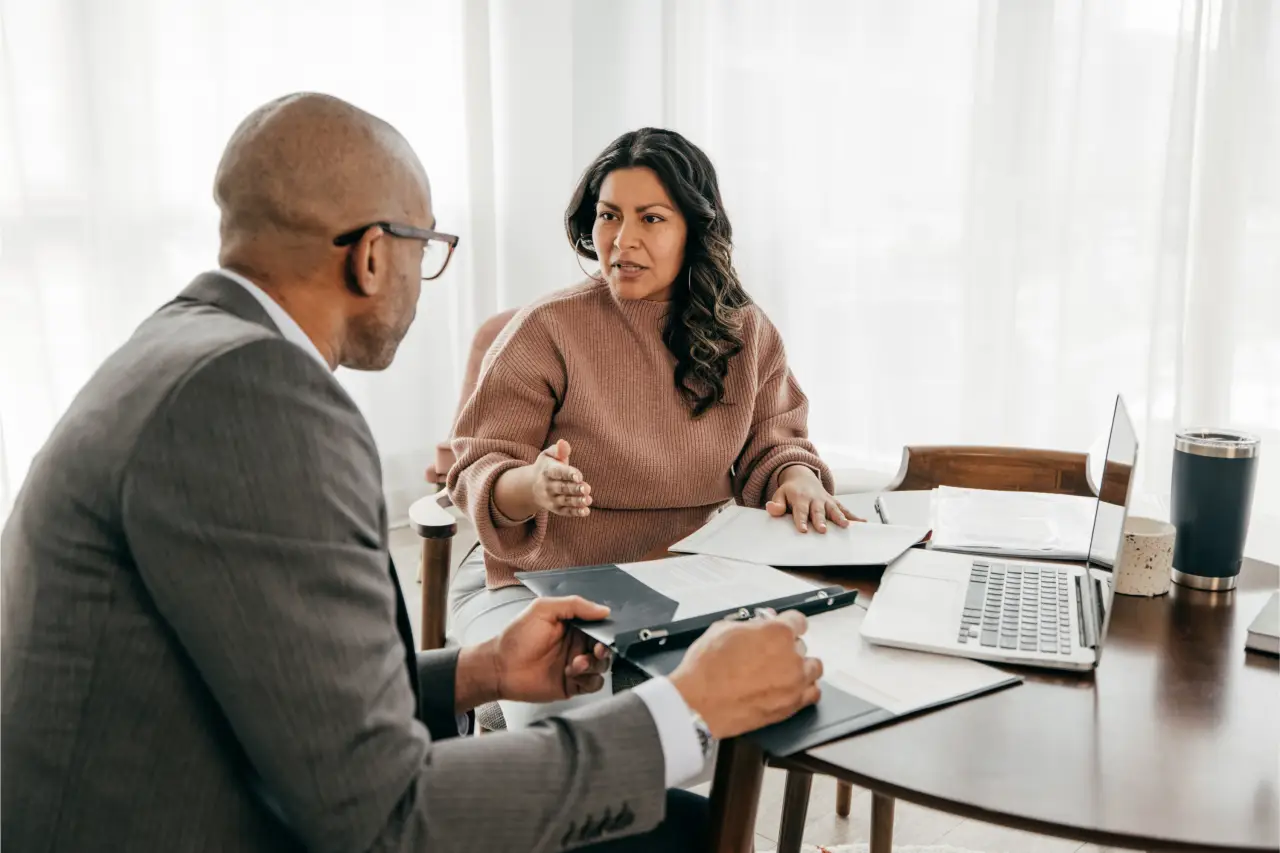 Two people in a serious discussion at a table with documents and a laptop.