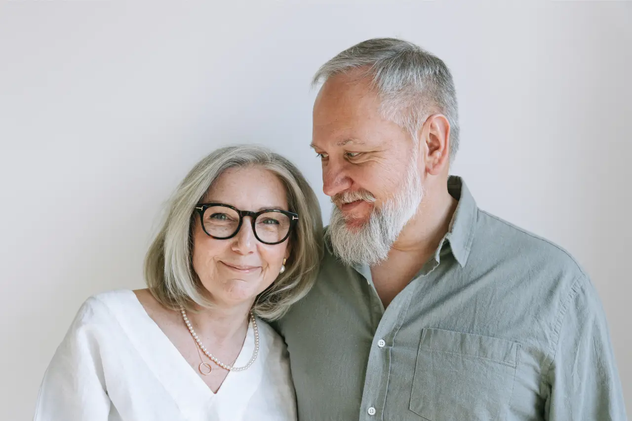 Smiling older couple standing close together against a plain light background.