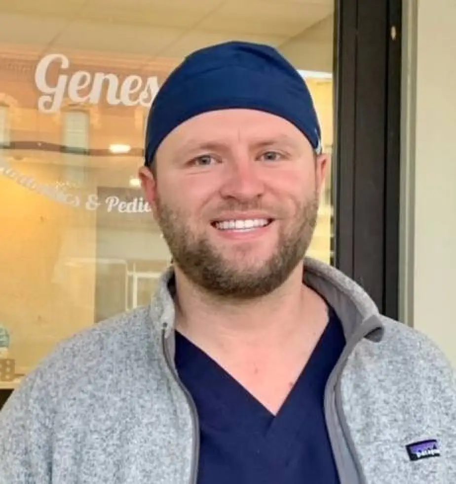 Smiling man in navy scrubs and cap stands outside a building with glass doors and signage.
