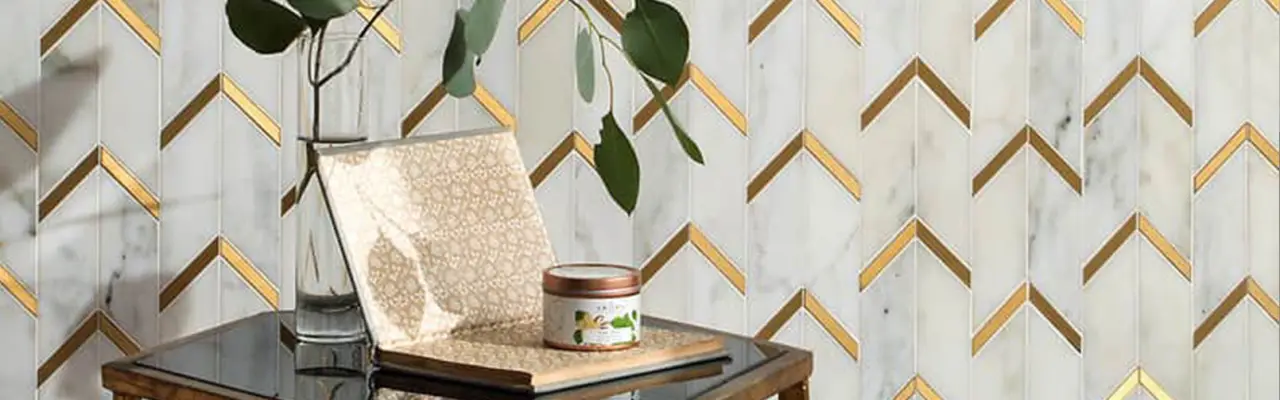 A side table with a book, candle, and vase in front of a gold and white chevron-patterned wall.