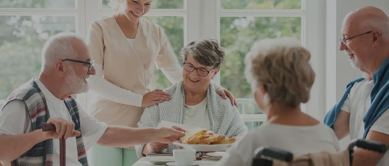 Caregiver serving a meal to smiling older adults at a table
