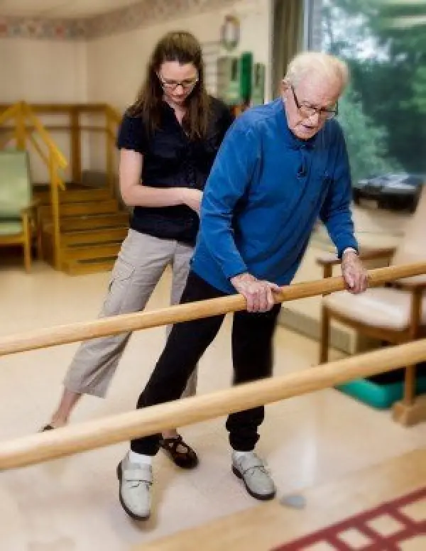 Therapist assisting an older adult with parallel bar walking exercises.