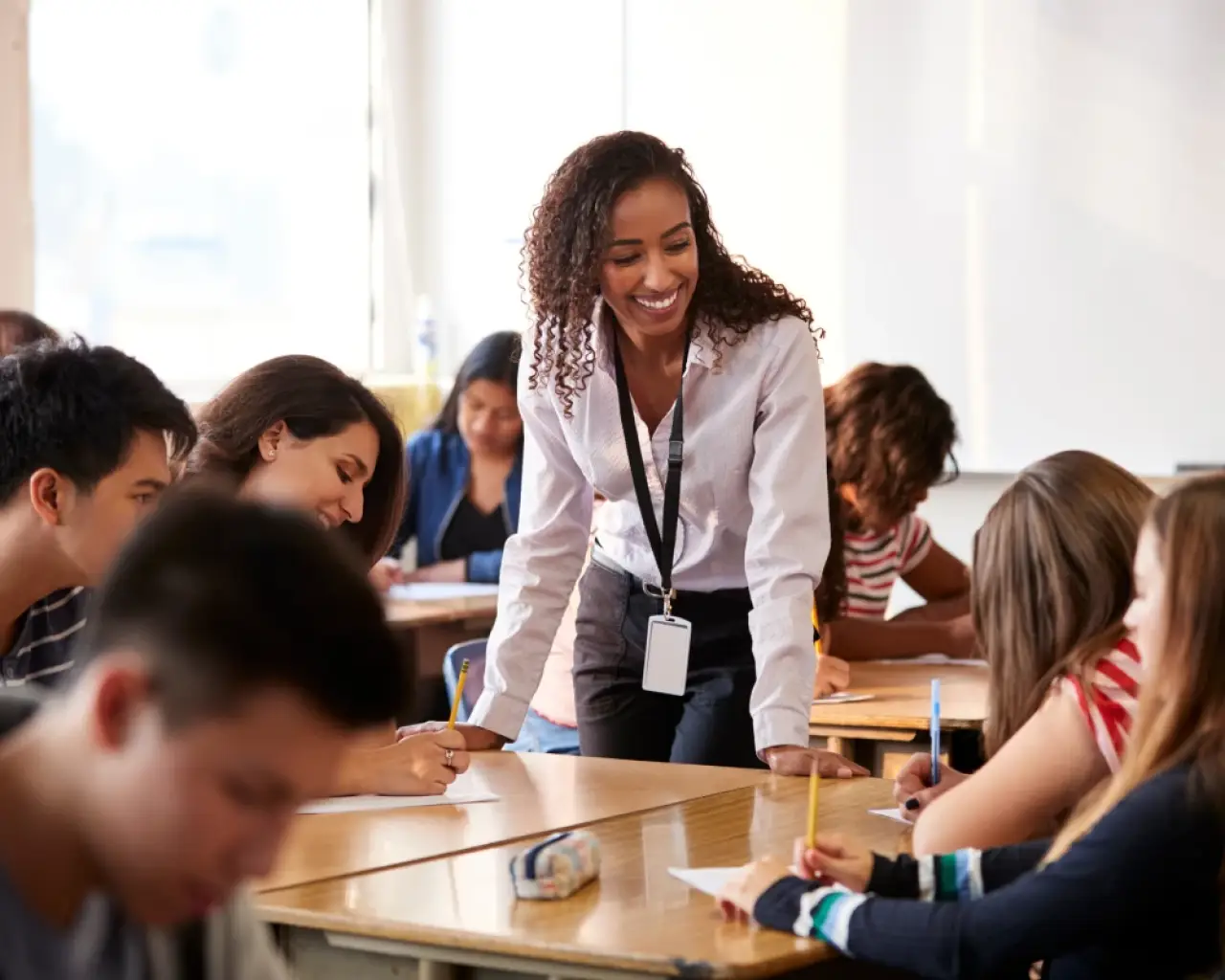 A long-term substitute teacher stands in the center of a classroom, with high school students sitting in desks that surround the teacher.