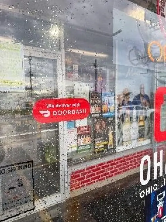 The image shows a window display for DoorDash in an Ohio location, featuring smoking and liquor promotions, with a warning sign about age restrictions.
AI-generated content may be incorrect.