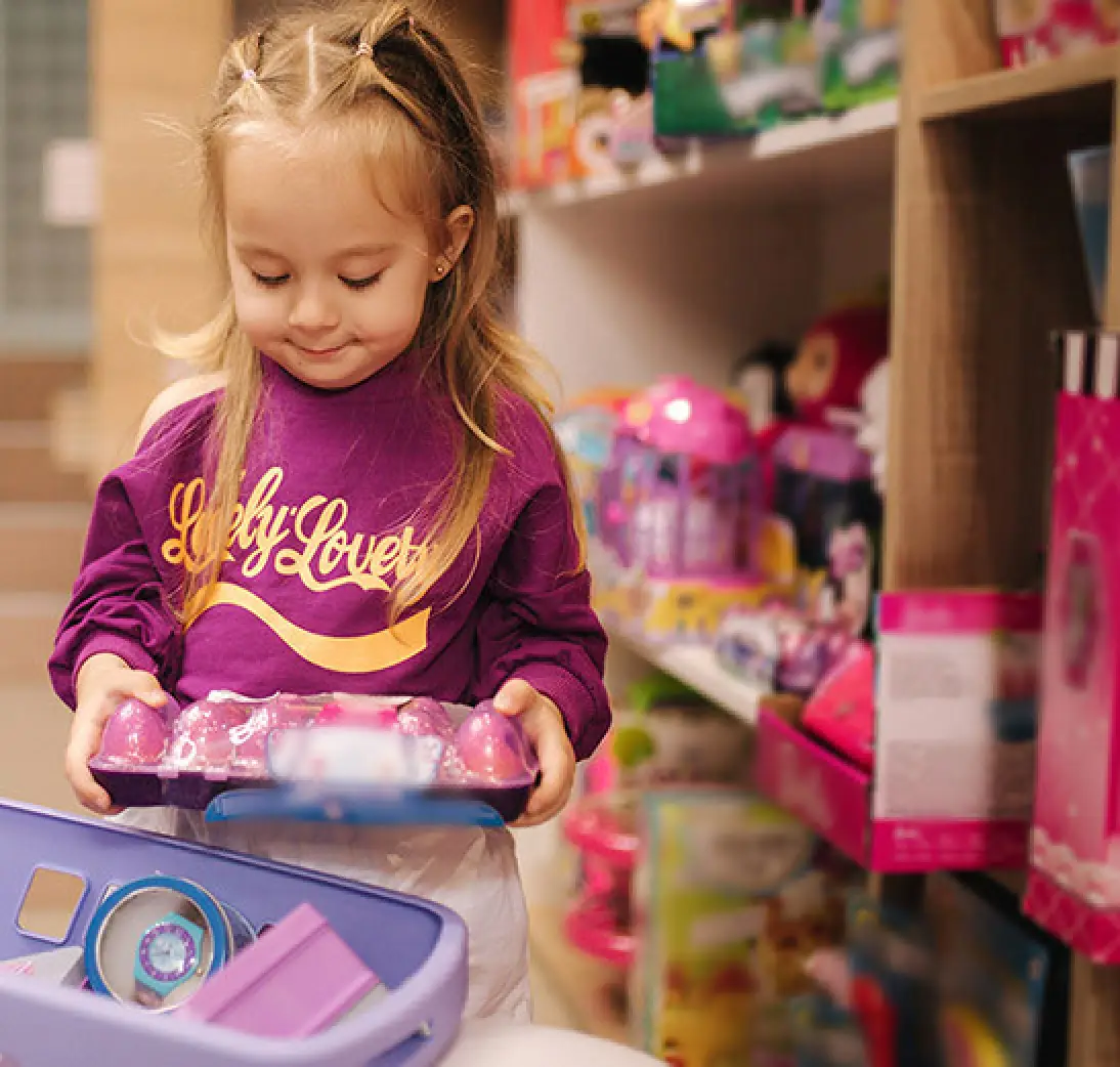 Young girl places a boxed toy into a shopping cart.