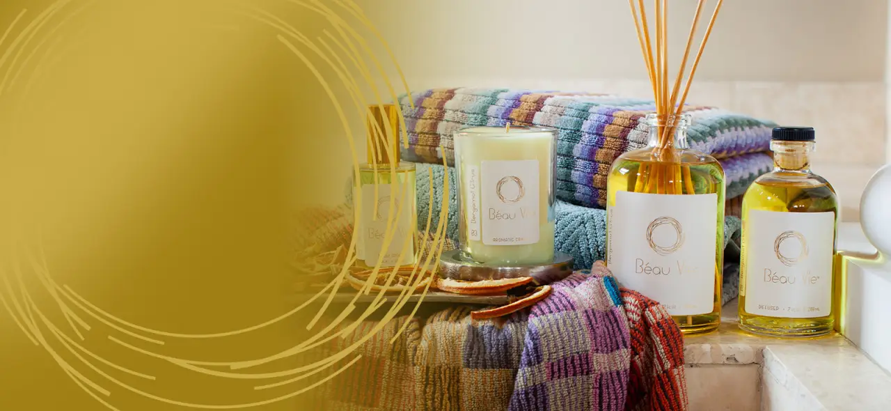Beau Vie candle, reed diffuser, and fragrance bottles beside colorful towels