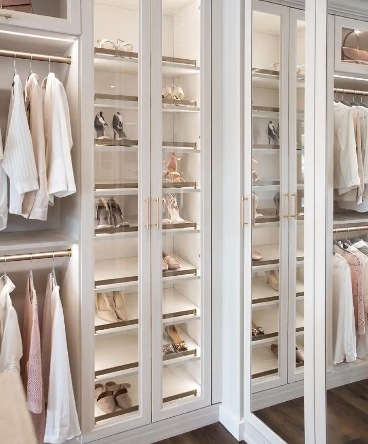 Spacious walk-in closet with shelves of shoes and hanging white and pastel clothing.