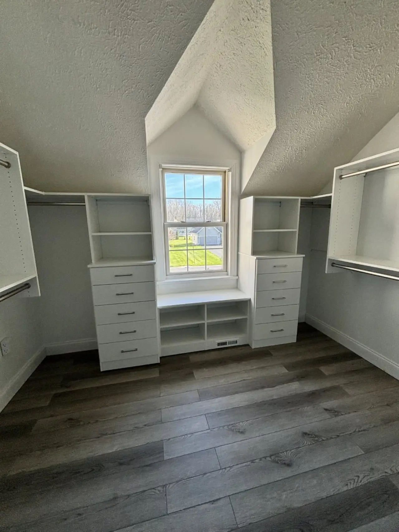 Bright walk-in closet with shelves, drawers, and a window overlooking a green yard.