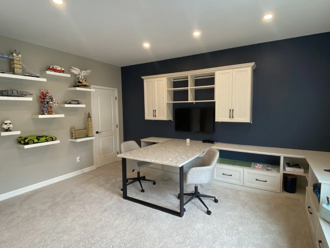 Modern home office with built-in cabinets, shelves of LEGO models, and two gray chairs.